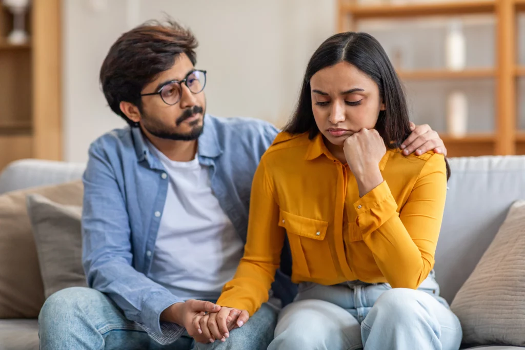 Man comforting woman on sofa while discussing visa overstay and marriage green card concerns